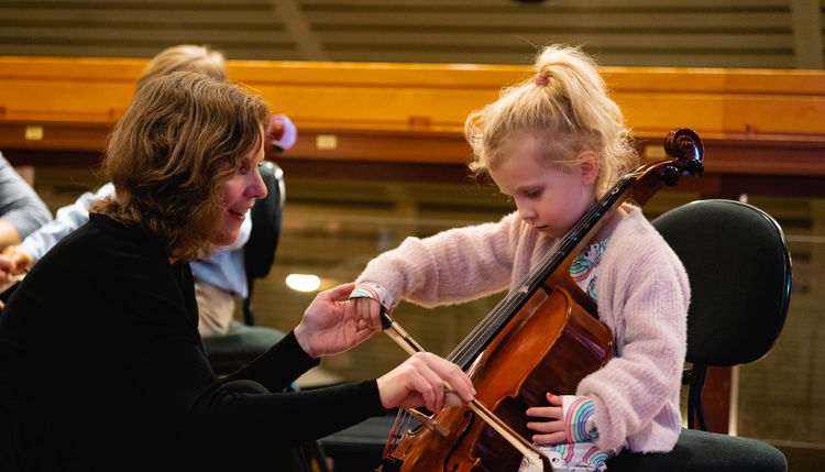 Et barn som spiller cello med hjelp fra en musiker fra Oslo-filharmonien